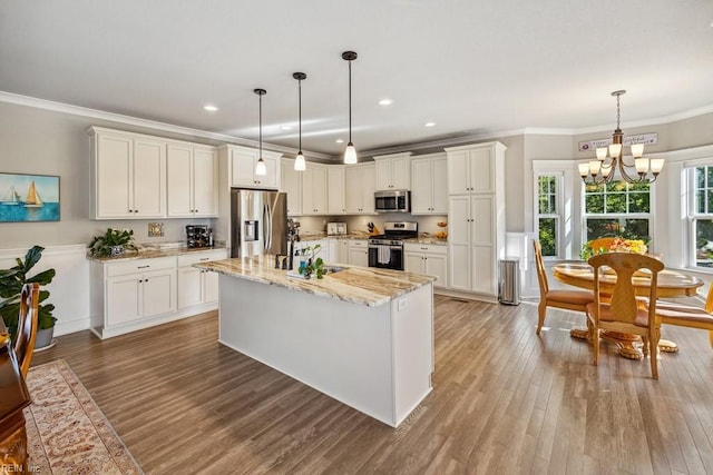 kitchen with white cabinets, light wood-type flooring, a notable chandelier, appliances with stainless steel finishes, and ornamental molding