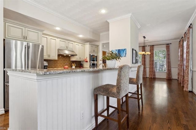 kitchen featuring a notable chandelier, cream cabinetry, under cabinet range hood, and stainless steel appliances