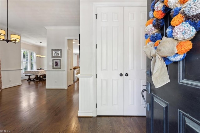 foyer featuring a wainscoted wall, an inviting chandelier, ornamental molding, and dark wood-style flooring