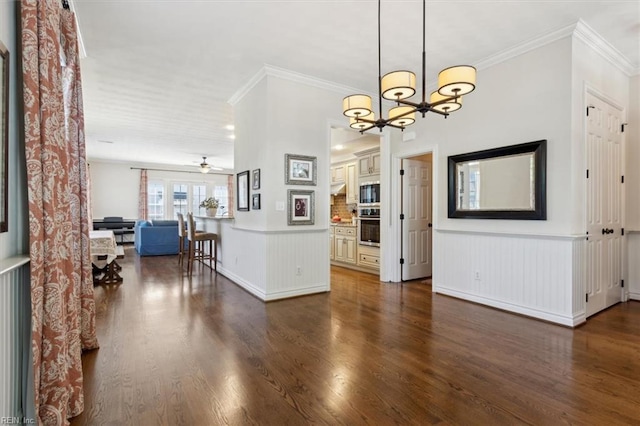interior space with ceiling fan with notable chandelier, a wainscoted wall, dark wood-style floors, and ornamental molding