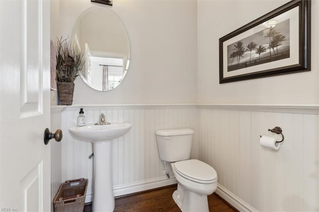 bathroom with wood finished floors, toilet, a sink, and wainscoting