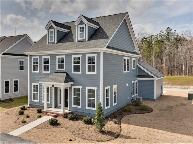 colonial inspired home with central AC, a shingled roof, and covered porch