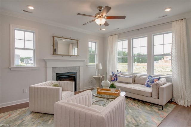 living room featuring wood finished floors, ceiling fan, a fireplace, ornamental molding, and visible vents