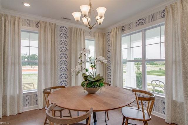 dining space featuring wallpapered walls, wood finished floors, visible vents, crown molding, and a notable chandelier