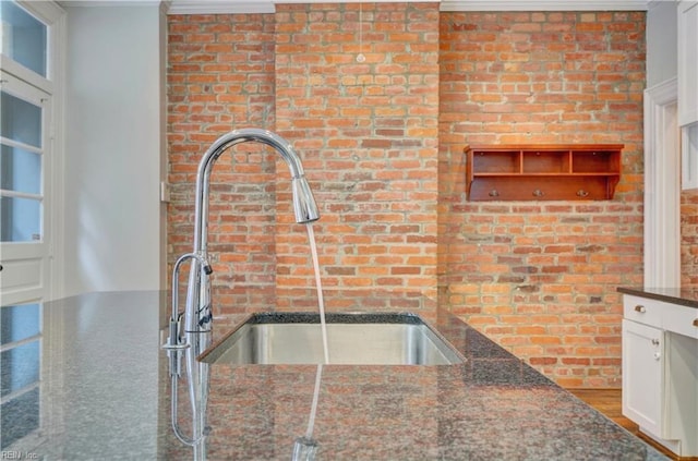 kitchen featuring dark stone countertops, crown molding, brick wall, and a sink