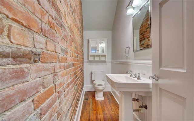 bathroom featuring brick wall, a wainscoted wall, wood finished floors, and toilet