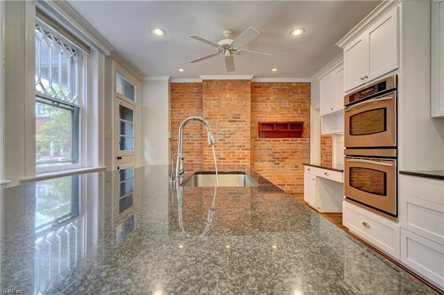 kitchen featuring double oven, brick wall, crown molding, and a sink