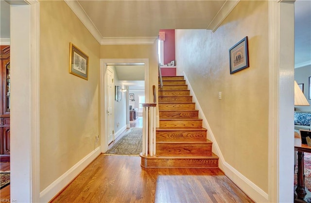 stairway with baseboards, crown molding, and wood finished floors