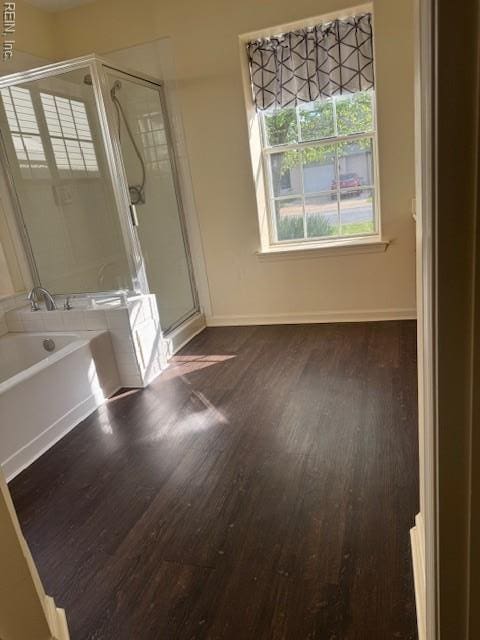 bathroom featuring baseboards, a garden tub, wood finished floors, and a shower stall