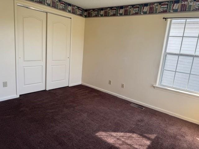 unfurnished bedroom featuring visible vents, dark colored carpet, baseboards, and a closet