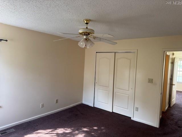 unfurnished bedroom featuring a textured ceiling, a closet, baseboards, dark colored carpet, and visible vents