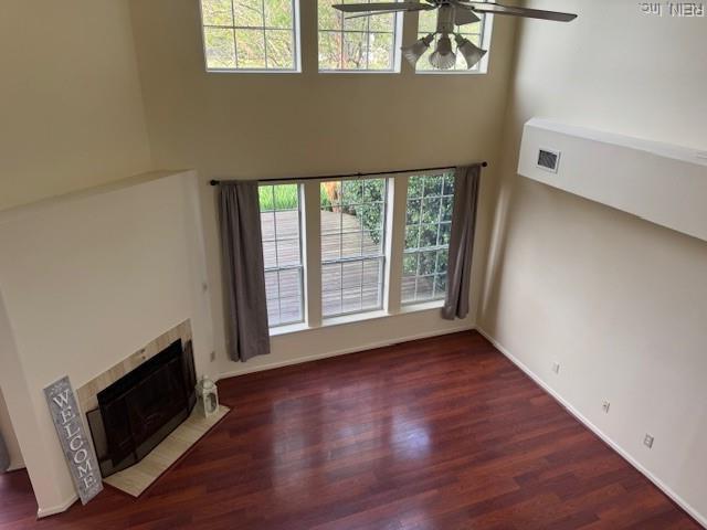 unfurnished living room with a healthy amount of sunlight, wood finished floors, a tile fireplace, and visible vents