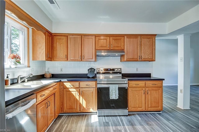 kitchen with under cabinet range hood, stainless steel appliances, a sink, decorative backsplash, and light wood-style flooring
