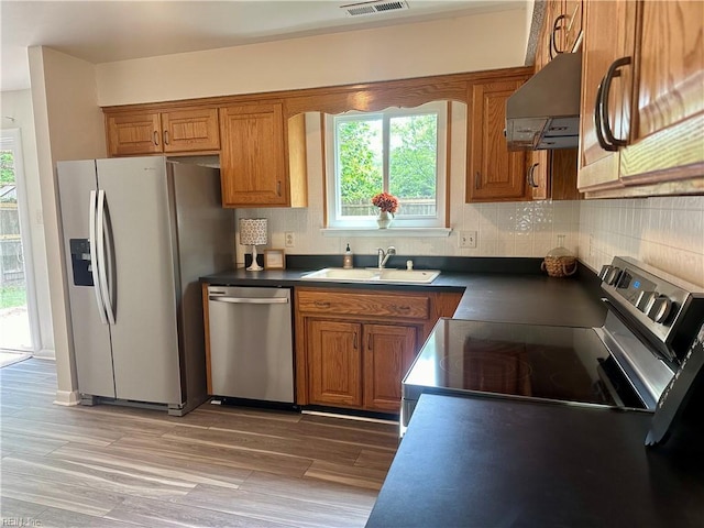 kitchen with brown cabinets, appliances with stainless steel finishes, under cabinet range hood, and a sink