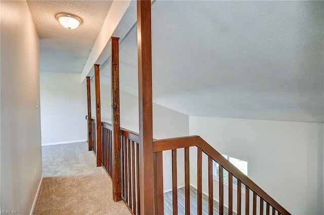 corridor featuring carpet, a textured ceiling, baseboards, and an upstairs landing