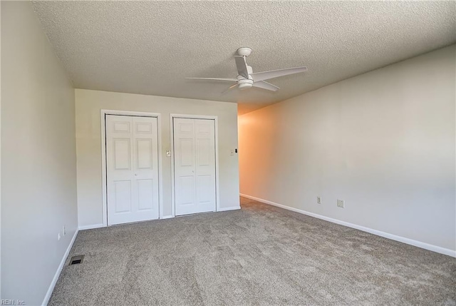 unfurnished bedroom featuring a textured ceiling, baseboards, visible vents, multiple closets, and carpet floors