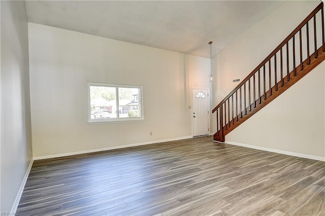 unfurnished living room featuring stairs, wood finished floors, and baseboards