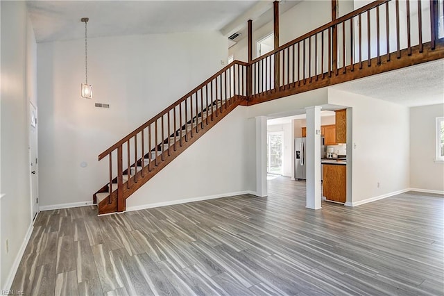 unfurnished living room featuring visible vents, wood finished floors, stairs, and a healthy amount of sunlight