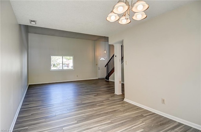 unfurnished living room with wood finished floors, stairs, baseboards, a notable chandelier, and visible vents