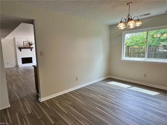unfurnished room featuring a textured ceiling, a chandelier, dark wood finished floors, baseboards, and visible vents