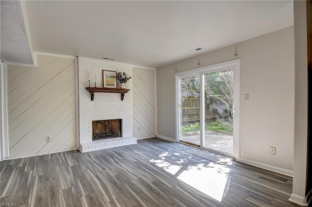 unfurnished living room featuring visible vents, baseboards, a brick fireplace, and wood finished floors