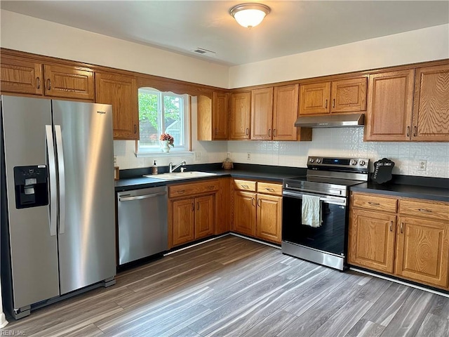 kitchen featuring brown cabinets, under cabinet range hood, stainless steel appliances, and a sink