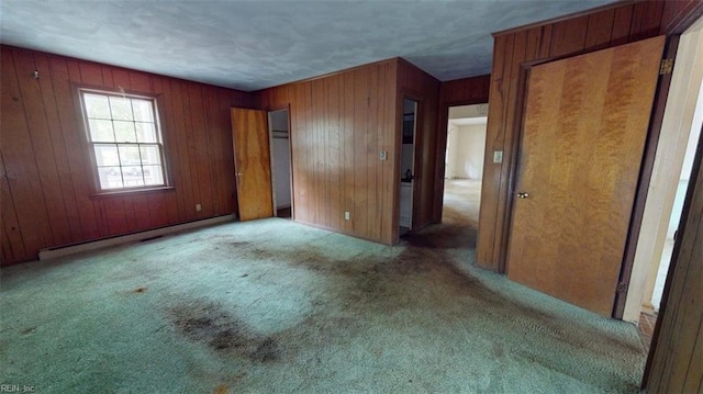 unfurnished bedroom with wooden walls, a baseboard heating unit, and carpet flooring