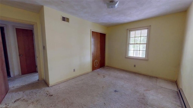 unfurnished bedroom featuring visible vents, baseboards, a closet, a baseboard heating unit, and carpet