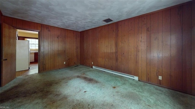 carpeted empty room with wood walls, baseboard heating, and visible vents