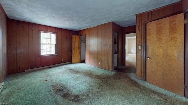 unfurnished bedroom featuring carpet flooring, wooden walls, and a baseboard heating unit