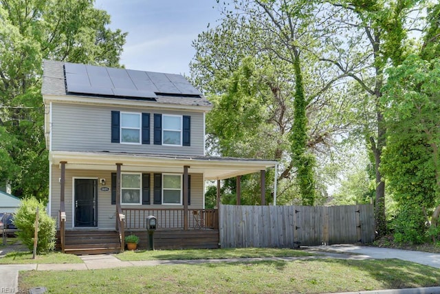 view of front facade with covered porch, a gate, fence, solar panels, and a front lawn