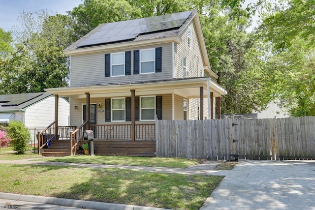view of front of property with roof mounted solar panels, a front yard, covered porch, and fence