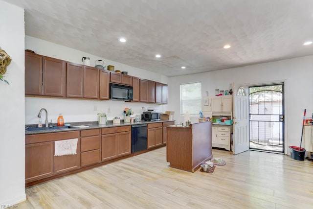 kitchen featuring a center island, black appliances, light wood finished floors, and a sink