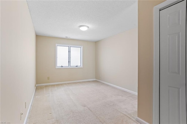empty room featuring a textured ceiling, baseboards, and light carpet