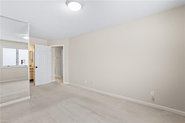 unfurnished bedroom featuring light carpet, a textured ceiling, and baseboards