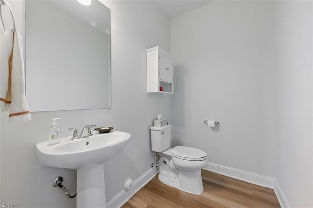 half bathroom with toilet, wood finished floors, and baseboards