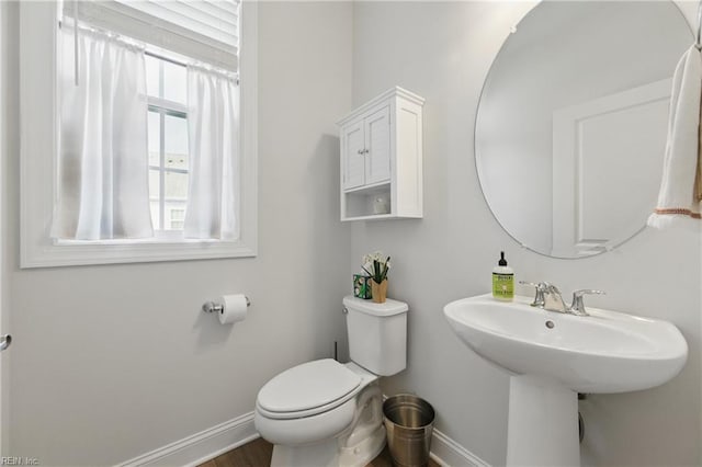 half bath with baseboards, wood finished floors, and toilet