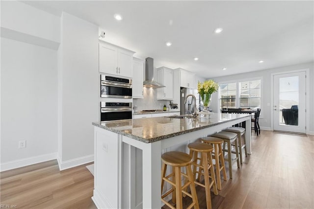 kitchen featuring light wood-style flooring, a large island, a sink, wall chimney exhaust hood, and a kitchen breakfast bar