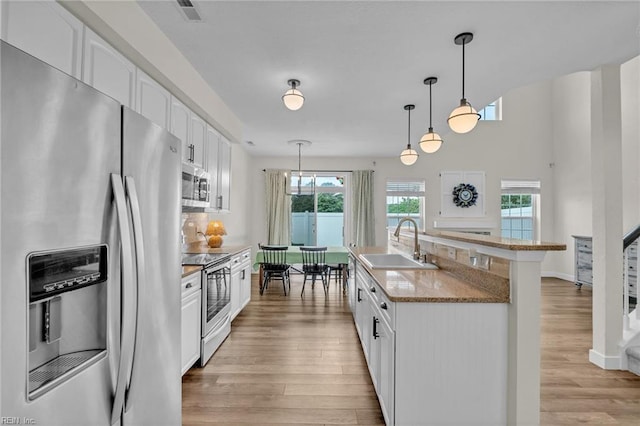 kitchen with a sink, light wood-type flooring, white cabinetry, decorative light fixtures, and appliances with stainless steel finishes