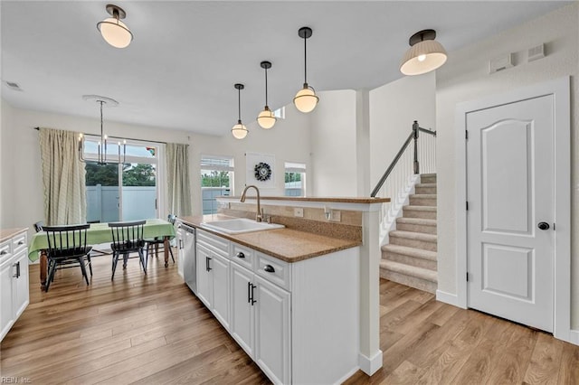 kitchen featuring stainless steel dishwasher, white cabinetry, a sink, and light wood finished floors