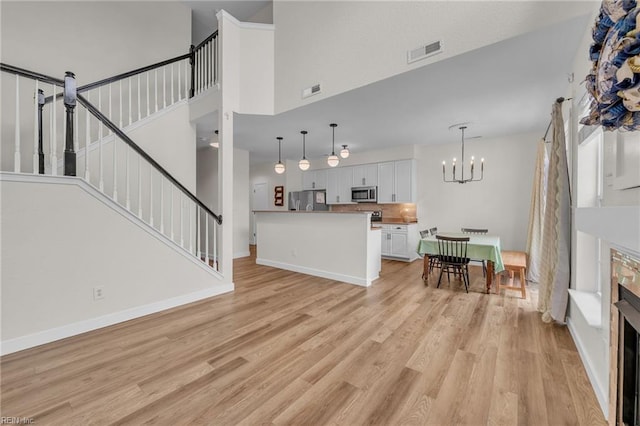 living area featuring stairway, a chandelier, light wood-type flooring, a fireplace, and visible vents