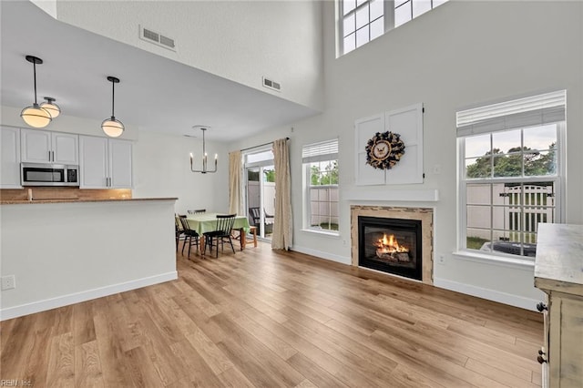 living room with an inviting chandelier, a glass covered fireplace, visible vents, and light wood-style flooring