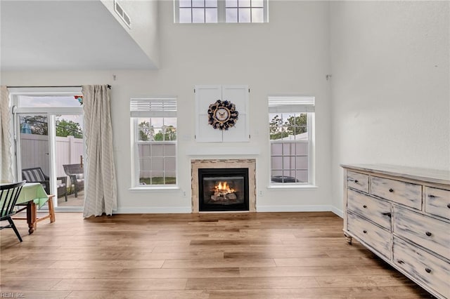 living room featuring a glass covered fireplace, wood finished floors, a towering ceiling, and baseboards