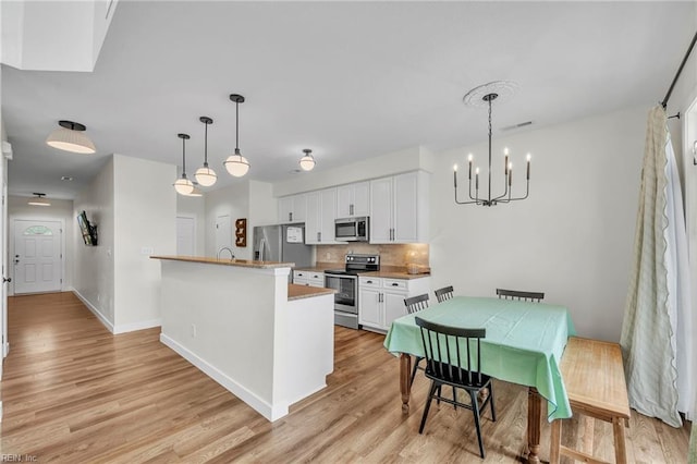 kitchen with tasteful backsplash, light wood-type flooring, appliances with stainless steel finishes, white cabinets, and a notable chandelier