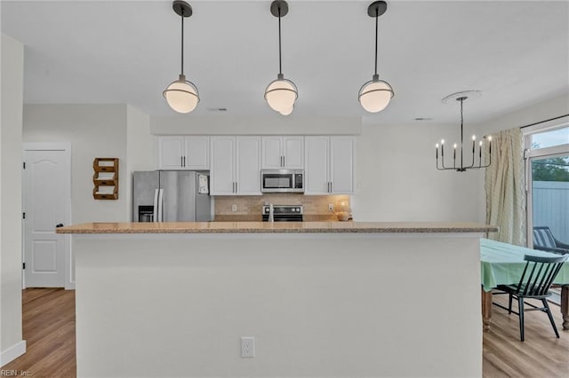 kitchen with an inviting chandelier, light wood finished floors, white cabinetry, backsplash, and appliances with stainless steel finishes