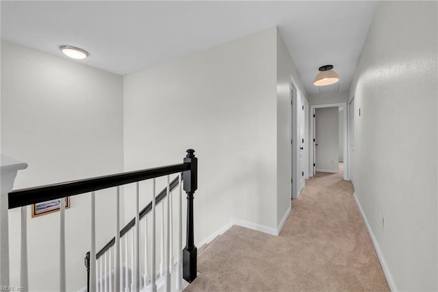hallway with light carpet, baseboards, and an upstairs landing