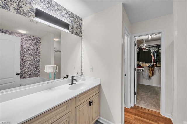 bathroom with a walk in closet, wood finished floors, baseboards, and vanity
