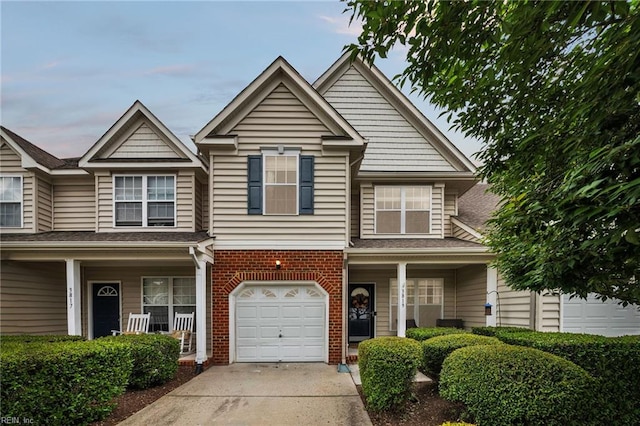 view of front of home featuring a porch, driveway, brick siding, and a garage