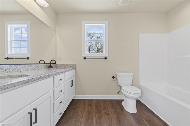 bathroom with wood finished floors, a sink, double vanity, baseboards, and toilet