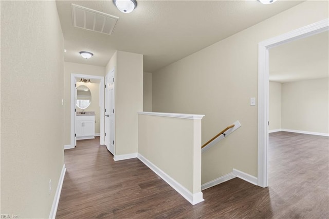 hallway featuring baseboards, wood finished floors, visible vents, and an upstairs landing